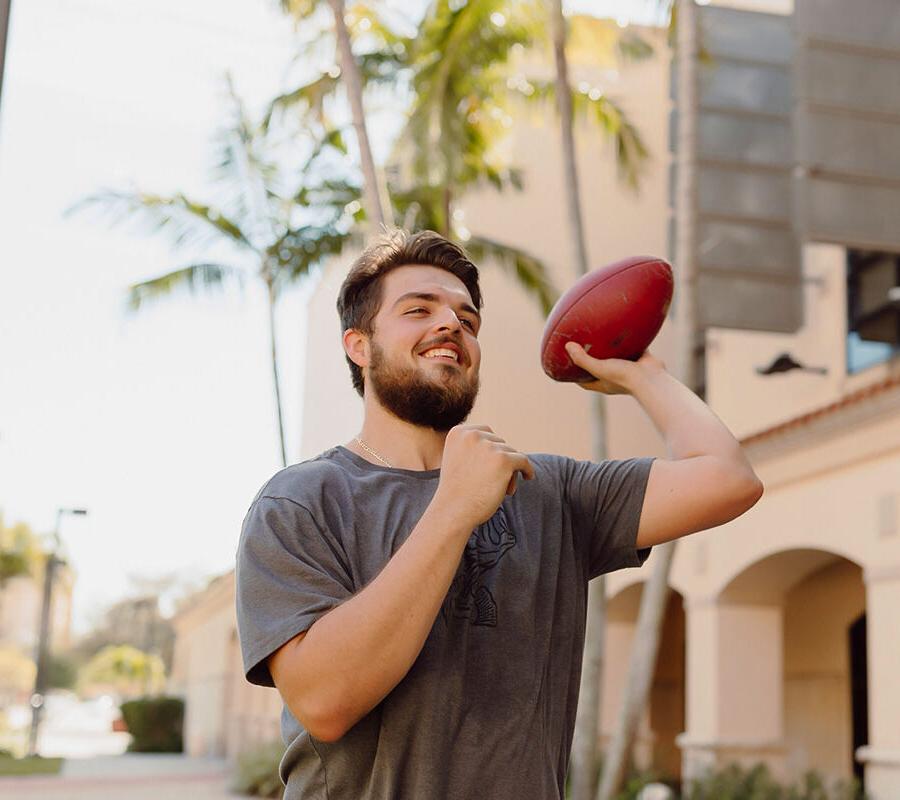 physical education student throws a football on campus.